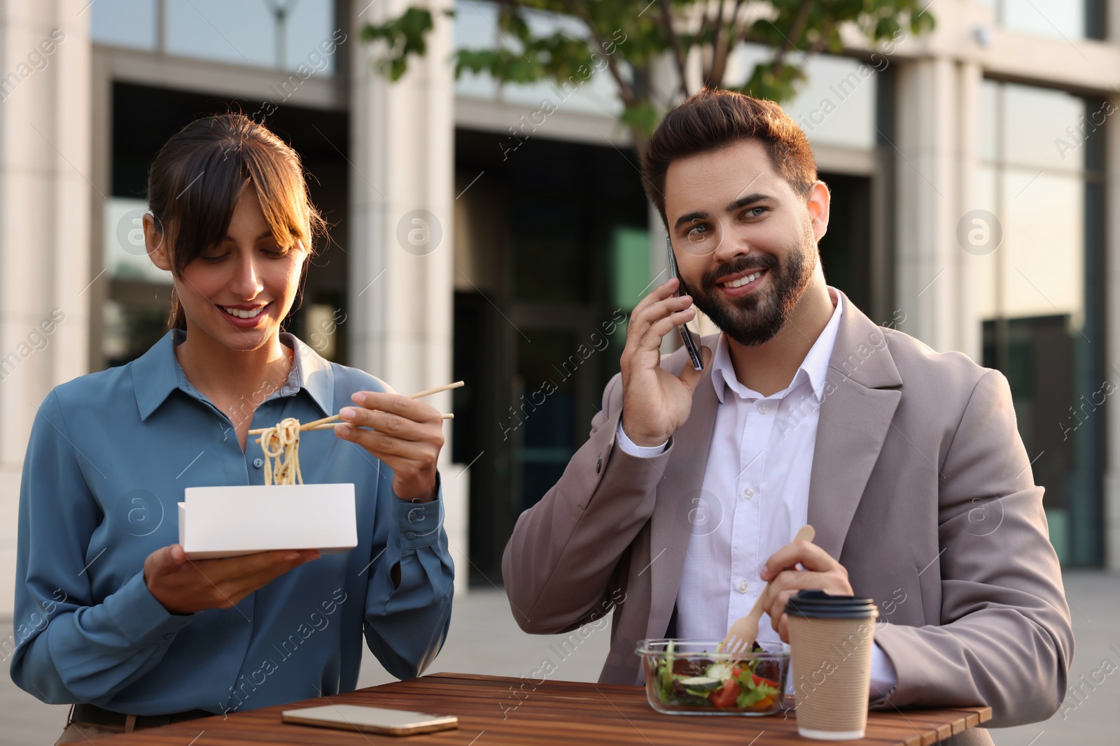 Photo of Happy colleagues having business lunch together at wooden table outdoors