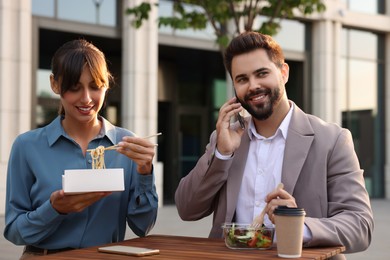 Photo of Happy colleagues having business lunch together at wooden table outdoors