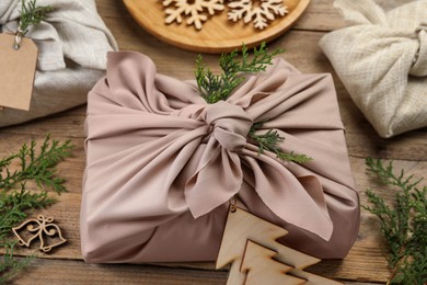 Photo of Furoshiki technique. Gift packed in fabric, thuja branches and festive decor on wooden table, closeup