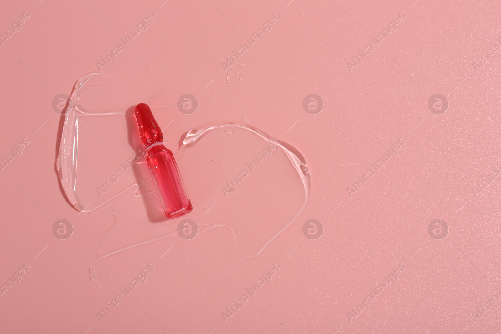 Photo of Skincare ampoule on pink surface with gel, top view. Space for text