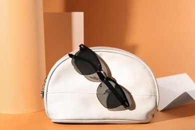 Photo of Stylish sunglasses and white makeup bag on pale orange background