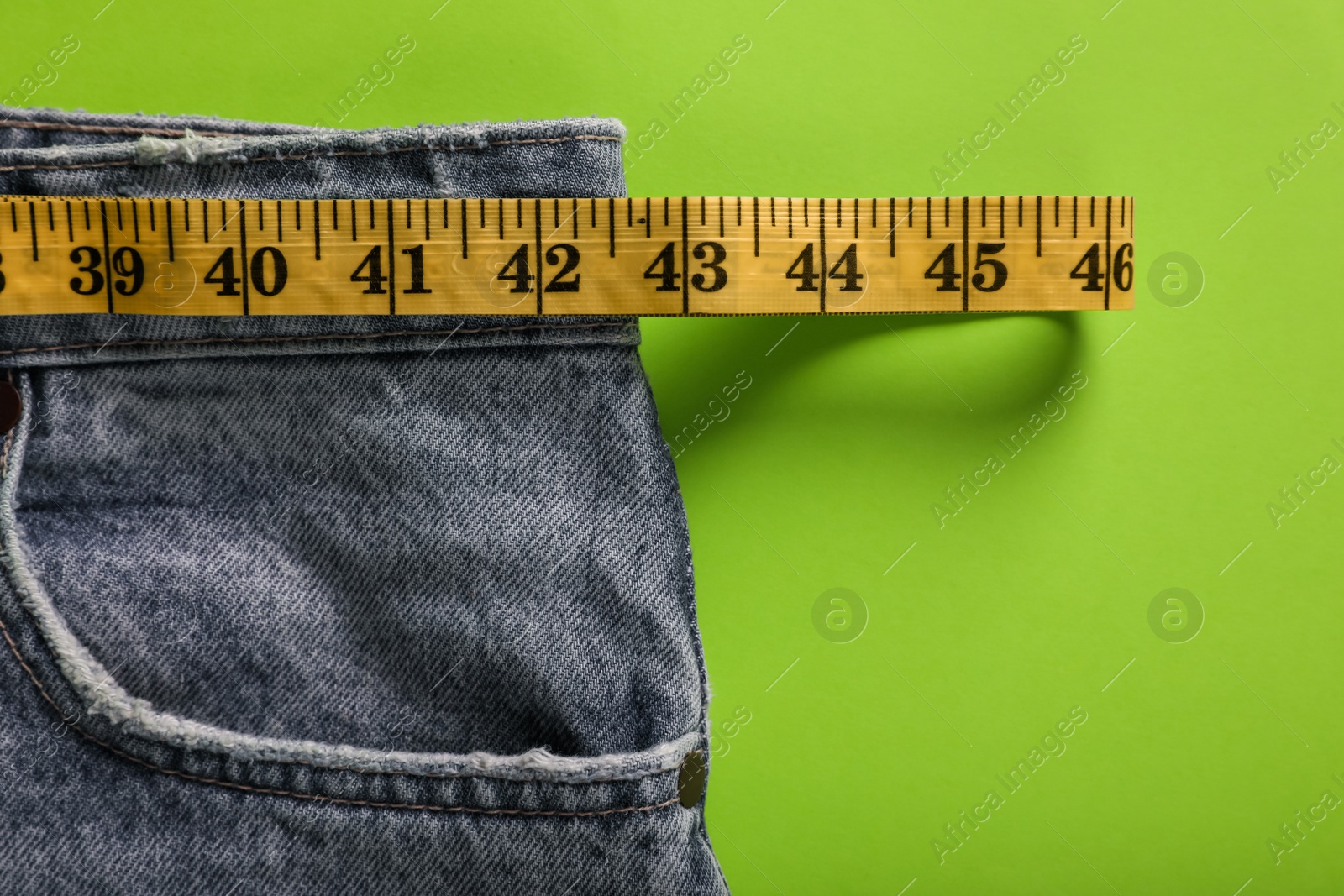 Photo of Jeans with measuring tape on green background, top view. Weight loss concept