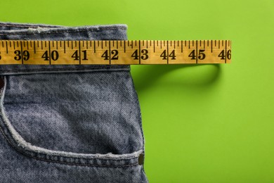 Photo of Jeans with measuring tape on green background, top view. Weight loss concept