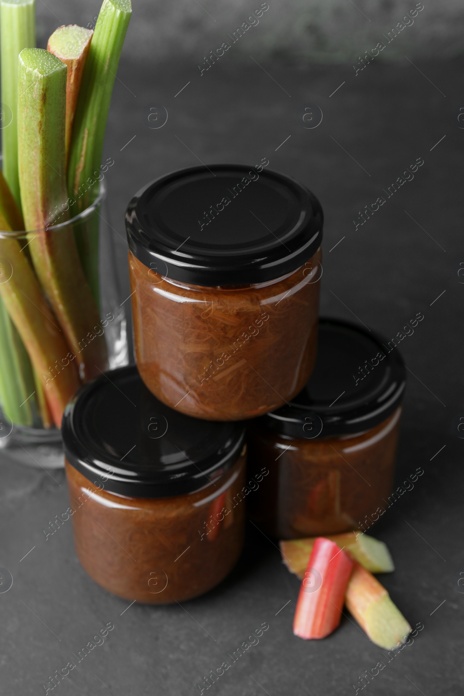 Photo of Jars of tasty rhubarb jam and stalks on grey table