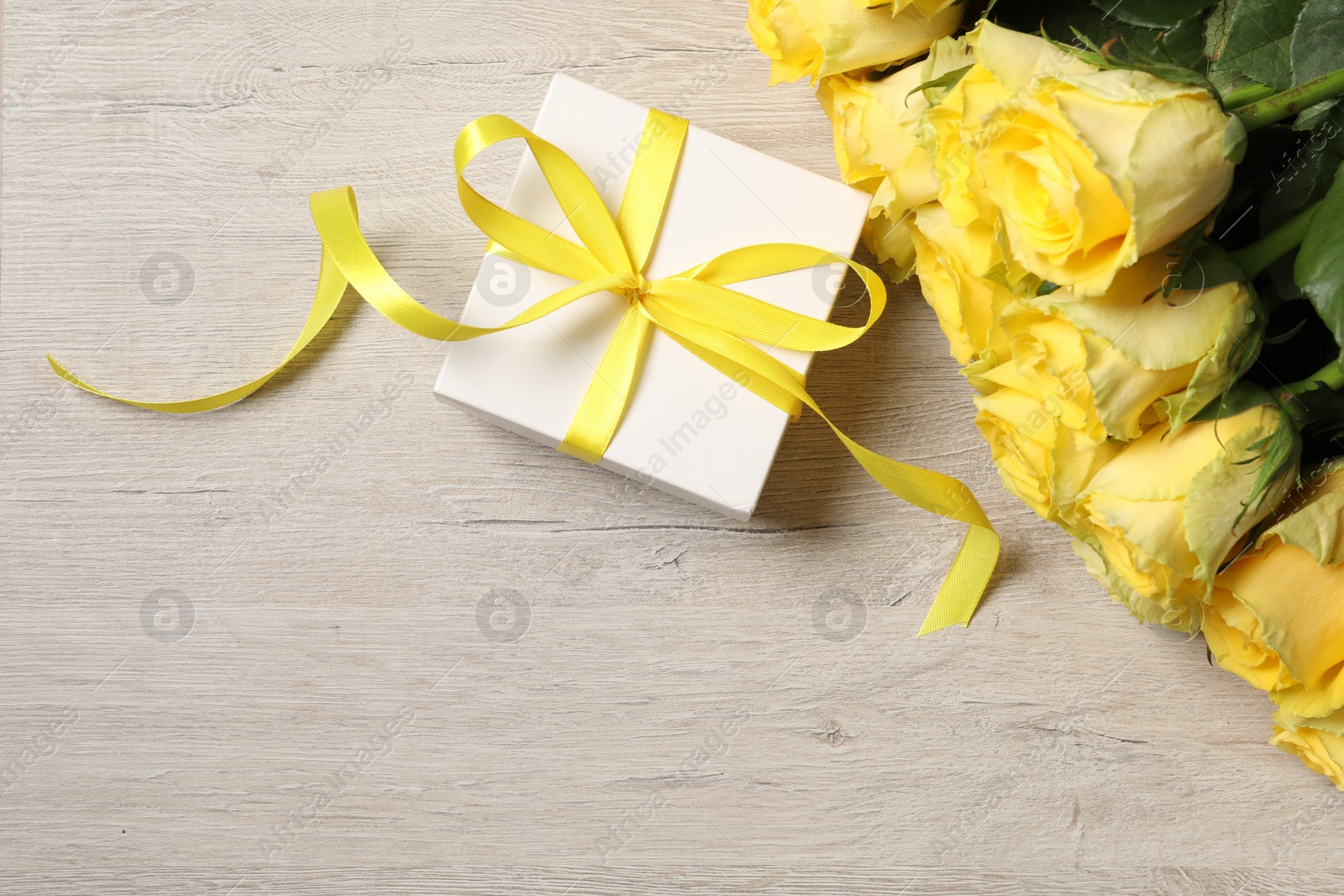 Photo of Beautiful bouquet of yellow roses and gift box on wooden table, flat lay. Space for text