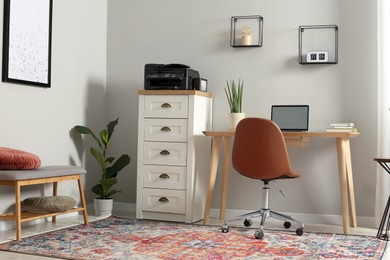 Photo of Stylish room interior with chest of drawers, modern printer and laptop