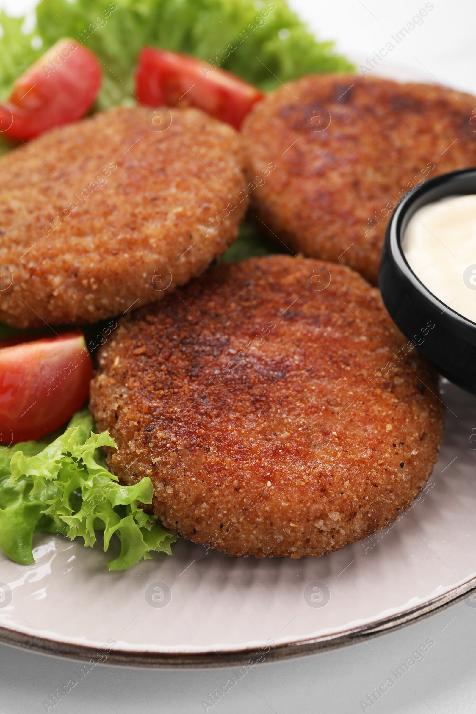 Photo of Delicious vegan cutlets, lettuce, tomato and sauce on white table, closeup