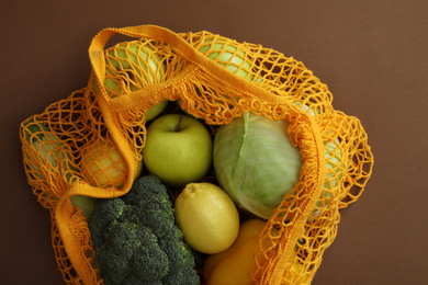 Photo of Net bag with fruits and vegetables on brown background, top view