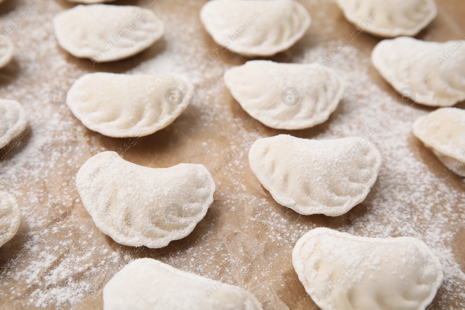 Photo of Raw dumplings (varenyky) with tasty filling and flour on parchment paper, closeup view