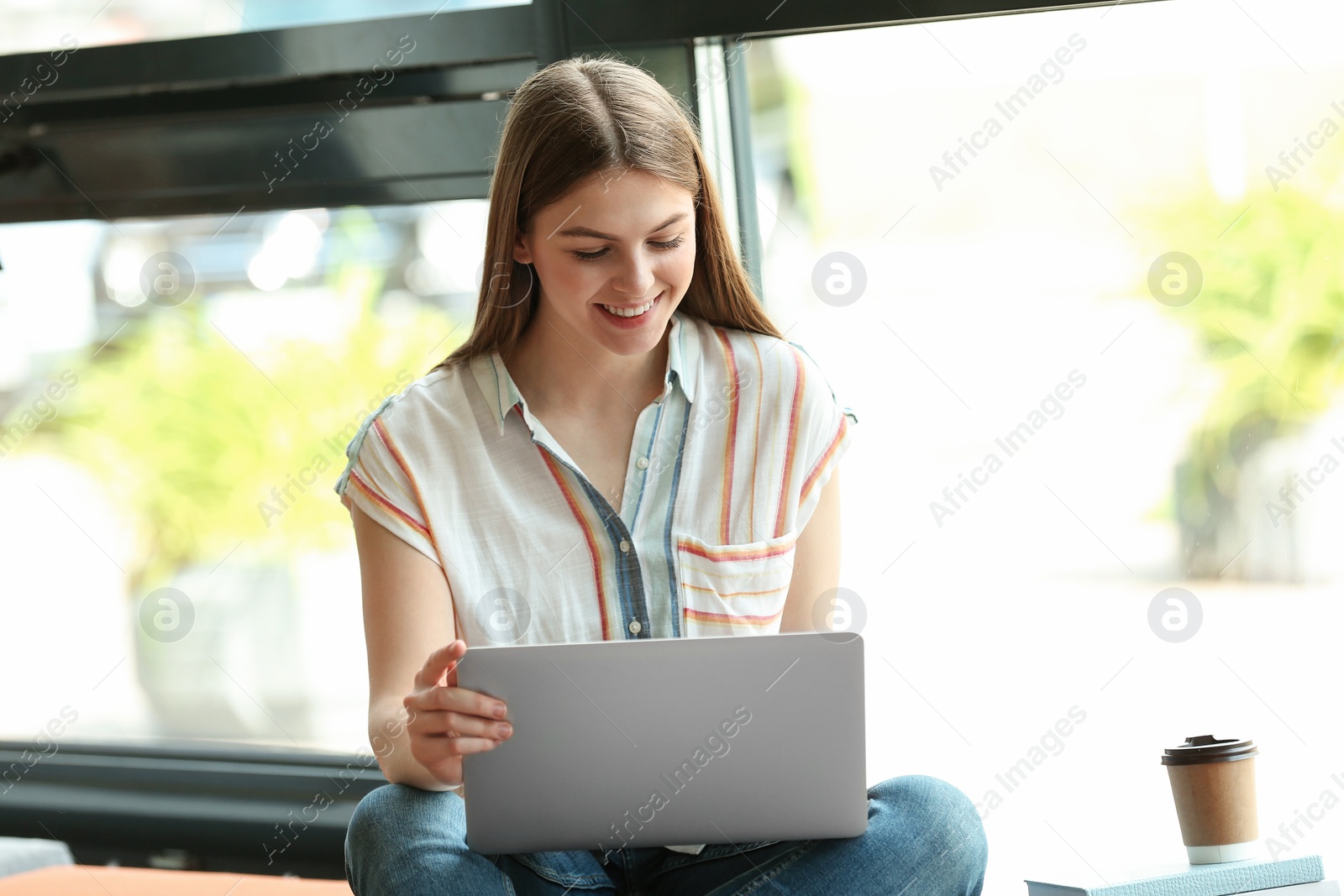 Photo of Young woman working on laptop near window in library