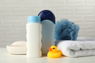 Photo of Baby cosmetic products, bath duck, sponge and towel on white table against brick wall