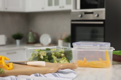 Containers with different fresh products, wooden board and knife on white marble table, space for text. Food storage