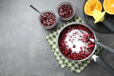 Photo of Making cranberry sauce. Fresh cranberries with sugar in saucepan and ingredients on gray table, flat lay. Space for text
