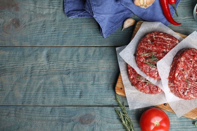 Flat lay composition with raw meat cutlets for burger on blue wooden table. Space for text