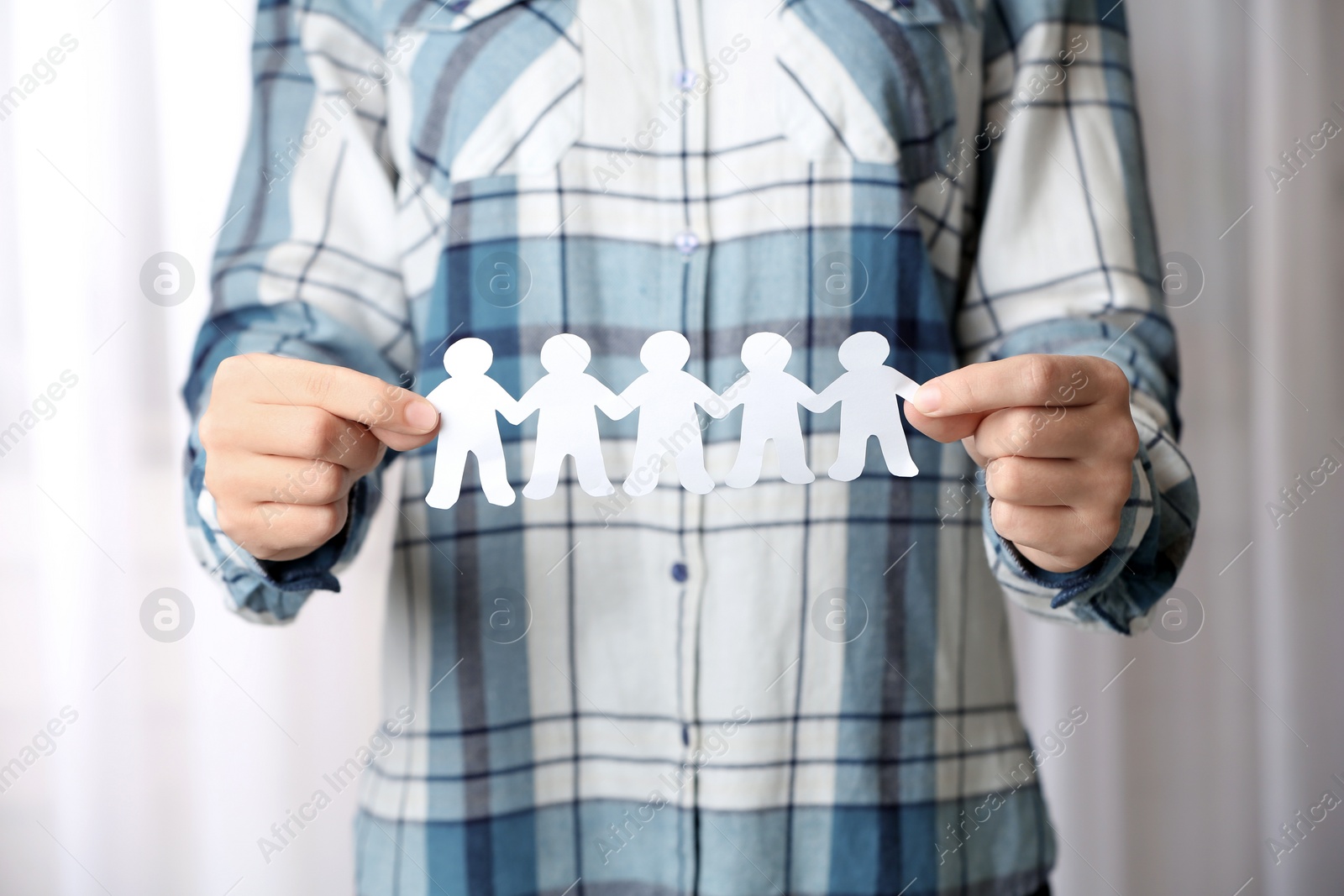 Photo of Woman holding paper people chain indoors, closeup. Unity concept