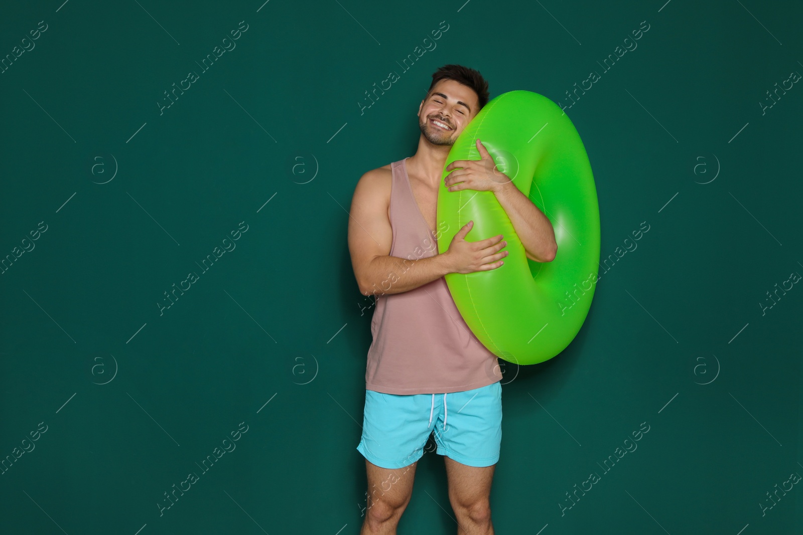 Photo of Funny young man with bright inflatable ring on dark green background, space for text