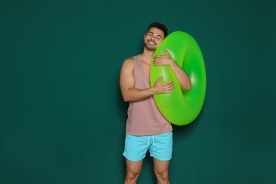 Funny young man with bright inflatable ring on dark green background, space for text