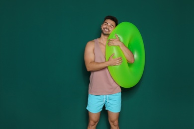 Photo of Funny young man with bright inflatable ring on dark green background, space for text