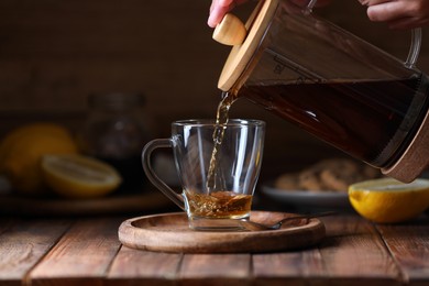 Photo of Woman pouring delicious tea into glass cup at wooden table, closeup
