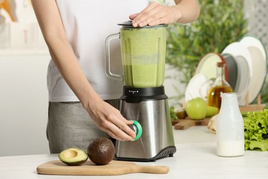 Photo of Woman preparing tasty green smoothie at white wooden table in kitchen, closeup