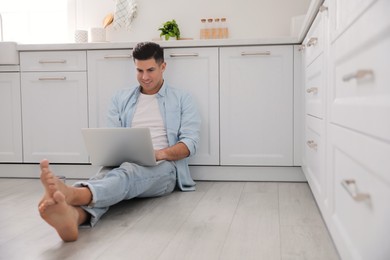 Photo of Man with laptop sitting on warm floor in kitchen, space for text. Heating system