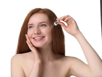 Smiling woman with freckles applying cosmetic serum onto her face against white background