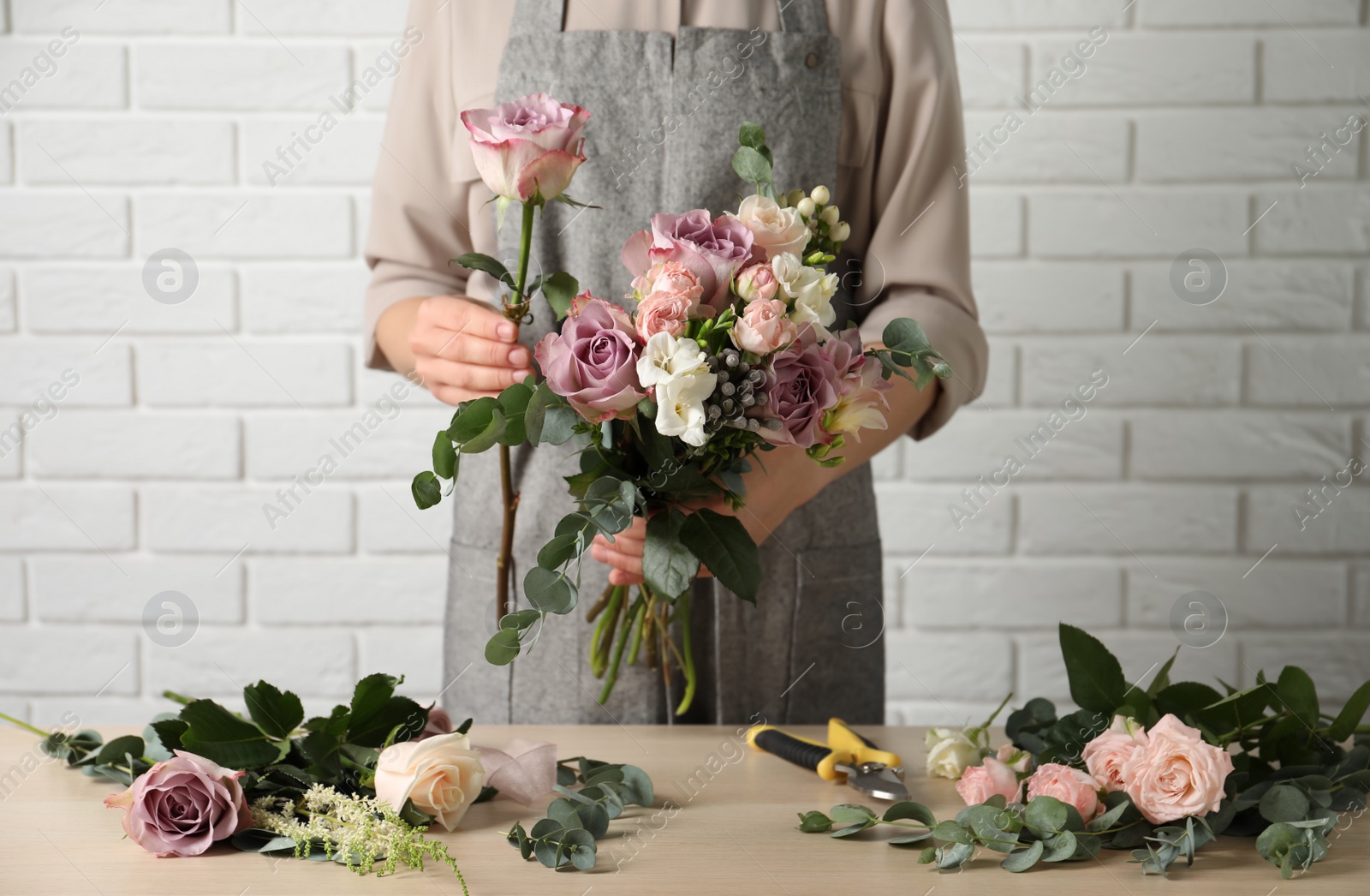 Photo of Florist creating beautiful bouquet at wooden table indoors, closeup