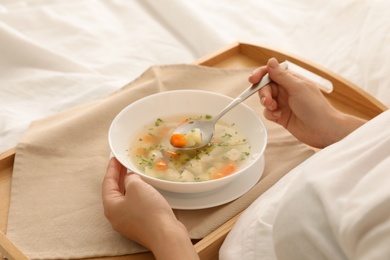 Sick woman eating fresh homemade soup to cure flu in bed at home, closeup