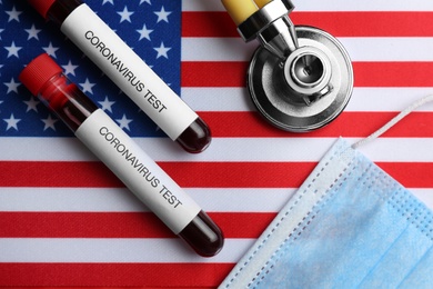 Photo of Test tubes with blood samples, medical mask and stethoscope on American flag, flat lay. Coronavirus pandemic in USA