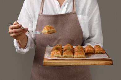 Woman with delicious sweet baklava on grey background, closeup