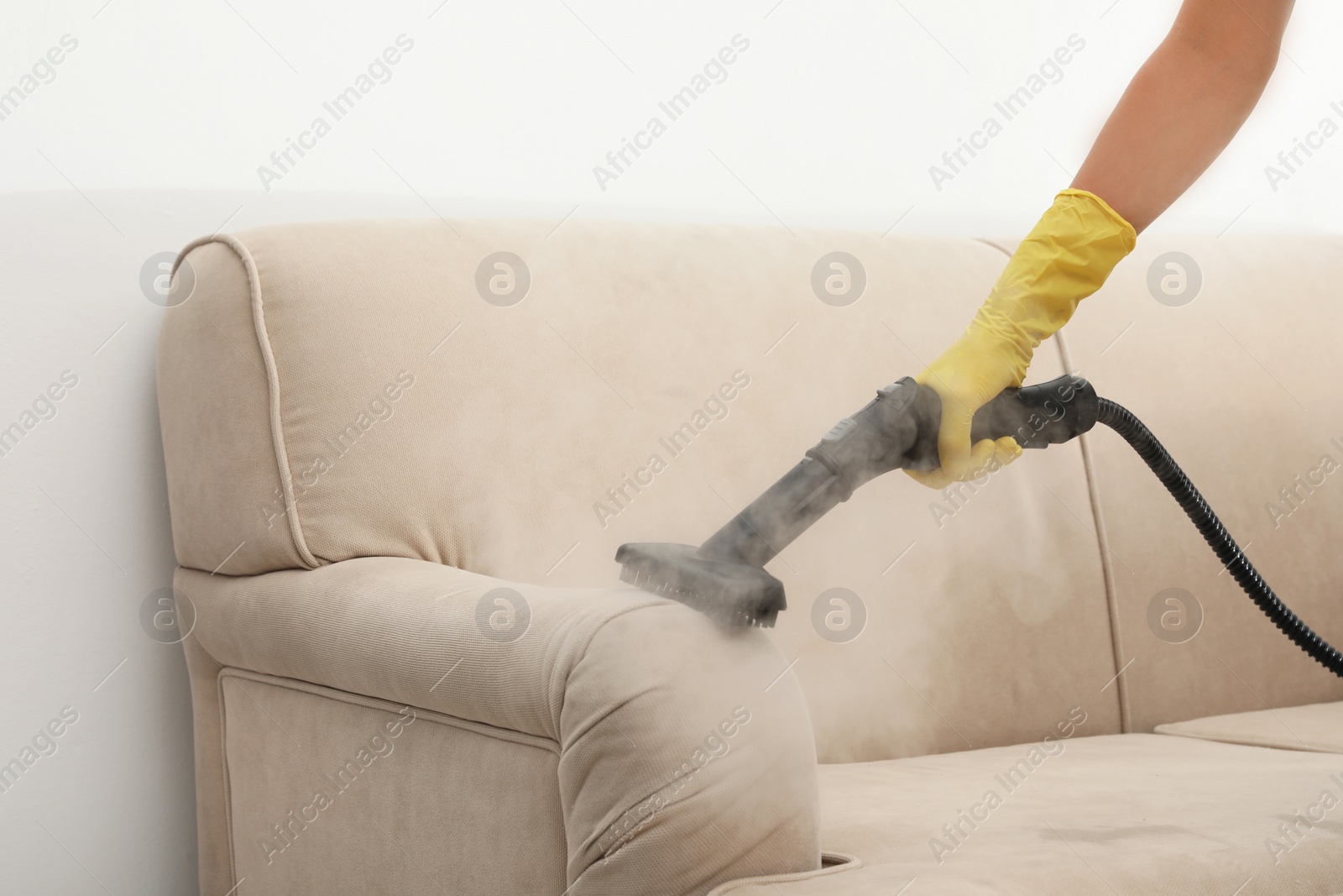 Photo of Janitor removing dirt from sofa with steam cleaner, closeup