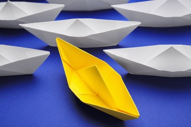 Photo of Yellow paper boat among others on blue background, closeup. Uniqueness concept