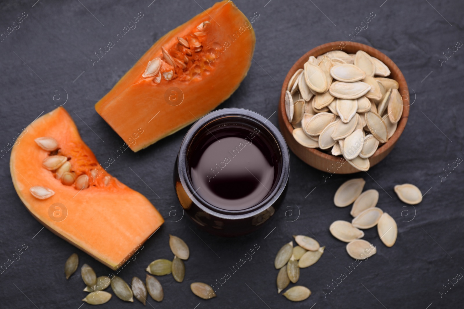 Photo of Flat lay composition with fresh pumpkin seed oil in glass jar on dark grey table