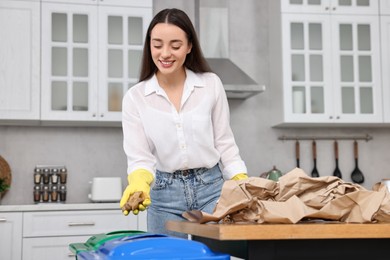 Photo of Garbage sorting. Smiling woman throwing potato peel into trash bin in kitchen
