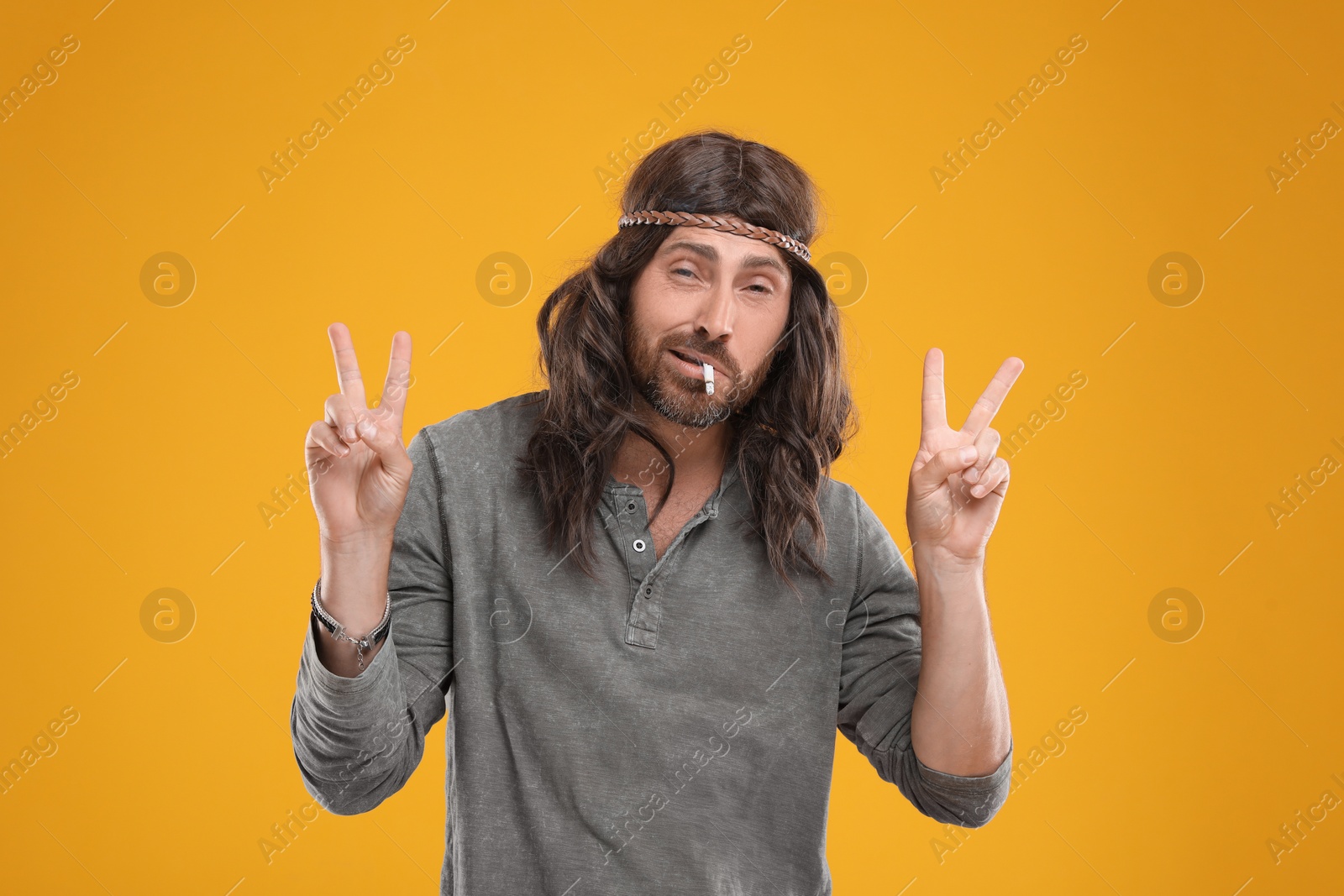 Photo of Hippie man smoking cigarette and showing V-sign on orange background