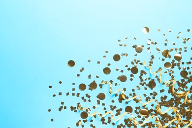 Photo of Shiny golden confetti and streamers on light blue background, flat lay