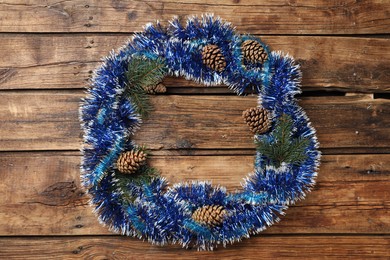 Photo of Frame of bright tinsel, fir tree branches and pine cones on wooden background, top view with space for text. Christmas decor