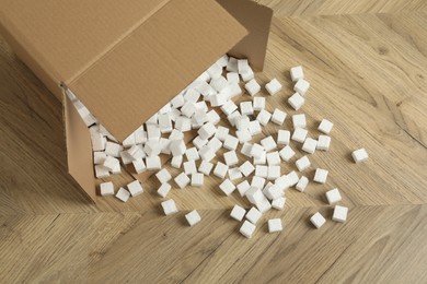 Photo of Overturned cardboard box with styrofoam cubes on wooden floor, above view