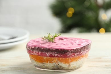 Photo of Herring under fur coat salad on white wooden table against blurred festive lights, space for text. Traditional Russian dish