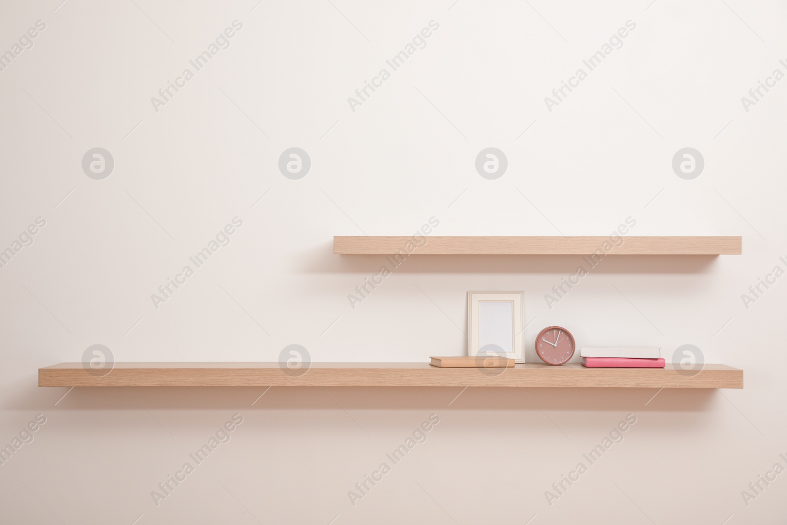 Photo of Wooden shelves with books, photo frame and clock on light wall