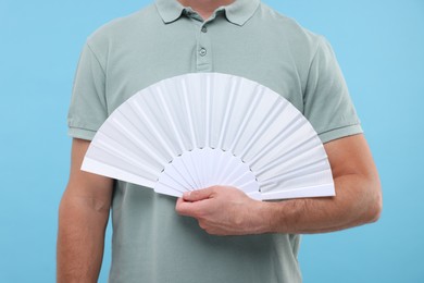 Photo of Man holding hand fan on light blue background, closeup