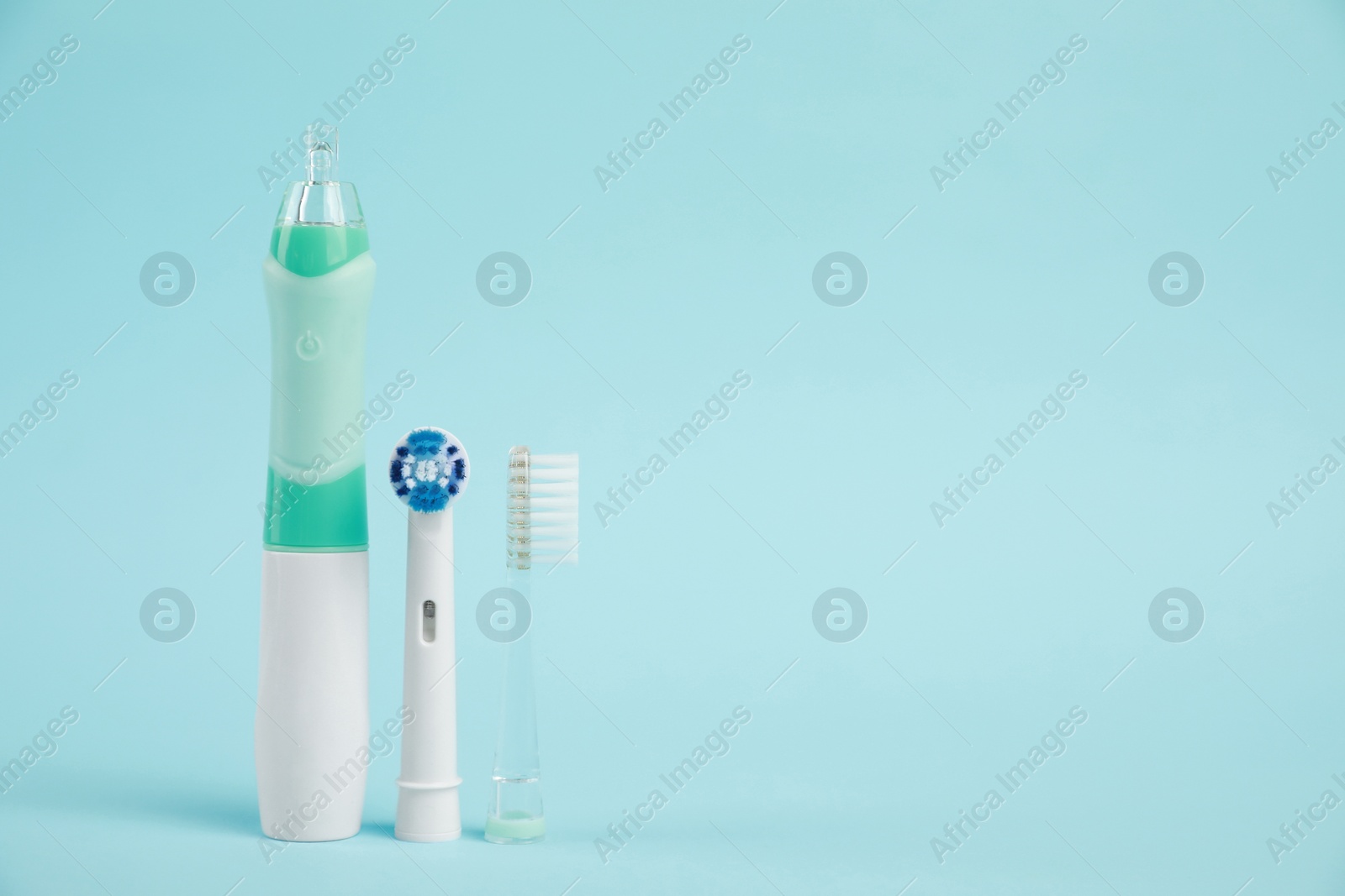 Photo of Electric toothbrush and replacement brush heads on light blue background, space for text