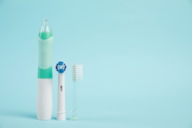 Electric toothbrush and replacement brush heads on light blue background, space for text