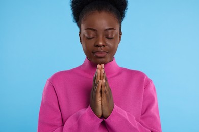 Woman with clasped hands praying to God on light blue background