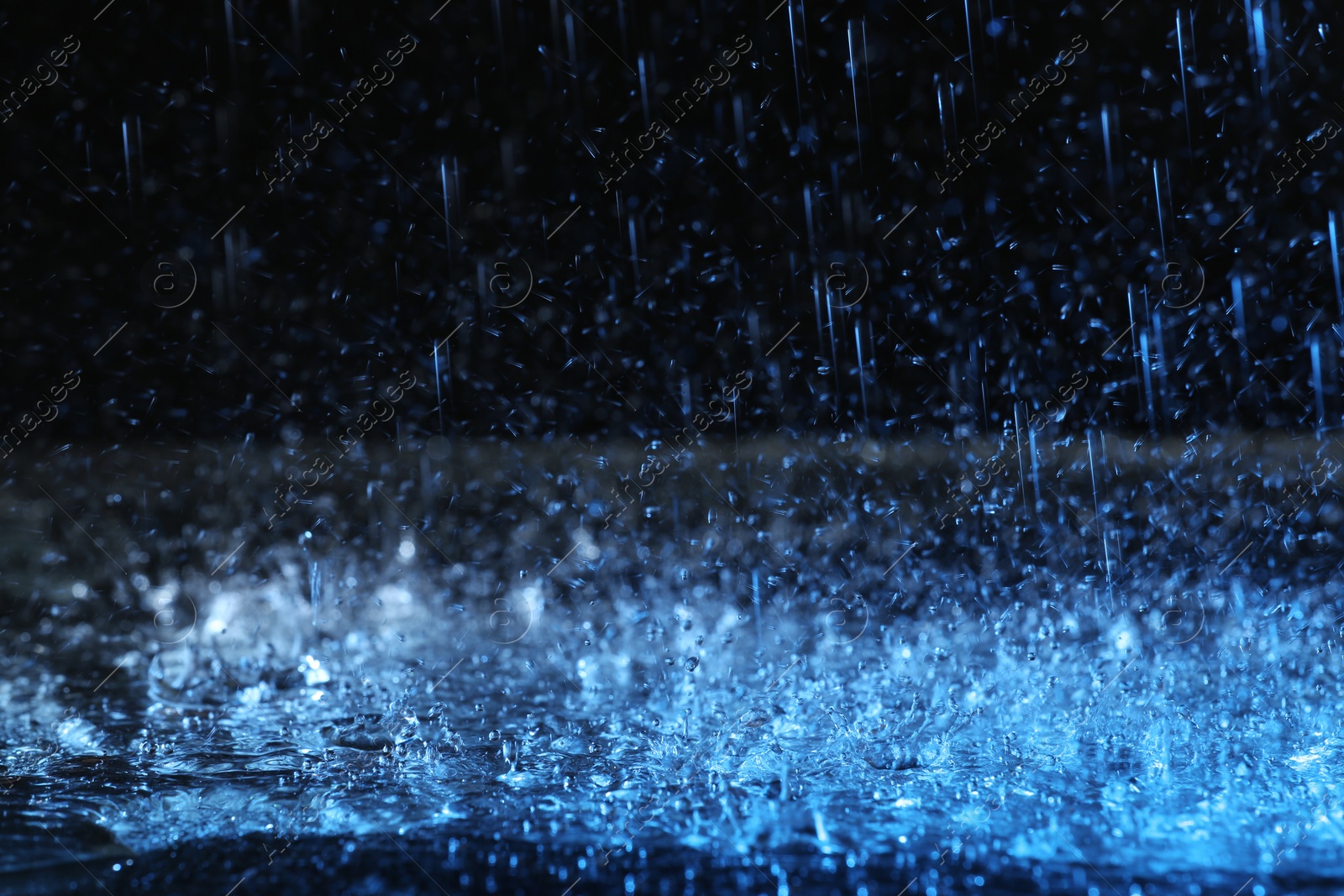 Photo of Heavy rain falling down on ground against dark background, toned in blue