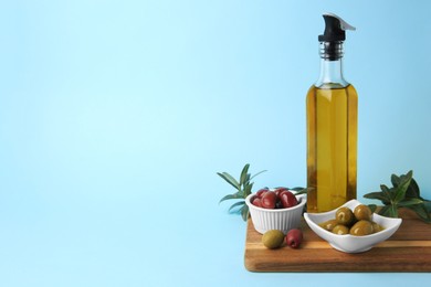 Photo of Bottle of oil, olives and tree twigs on light blue background, space for text