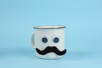 Photo of Man's face made of cup, fake mustache and decorative eyes on light blue background