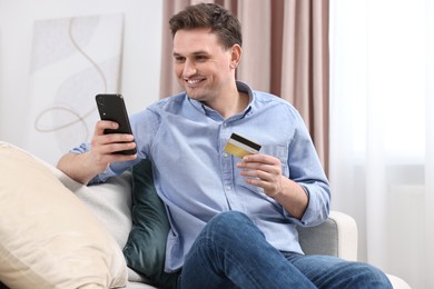 Photo of Happy man with credit card and smartphone shopping online at home