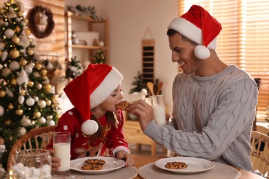 Happy father and his daughter eating delicious Christmas cookies at home