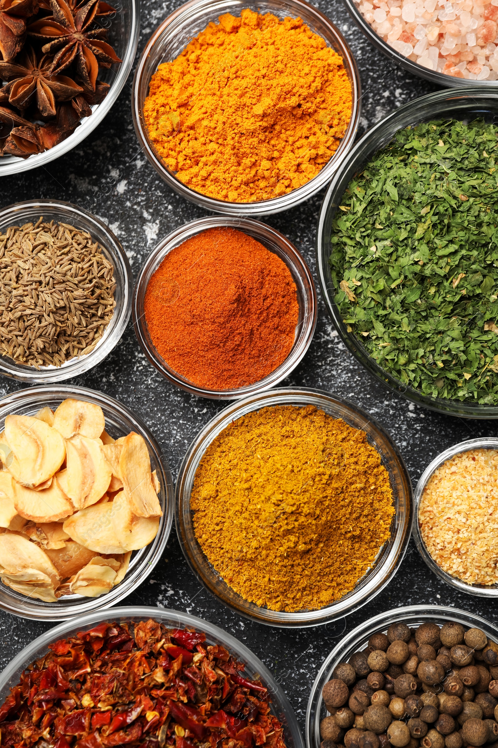 Photo of Glass bowls with different spices on grey textured table, flat lay